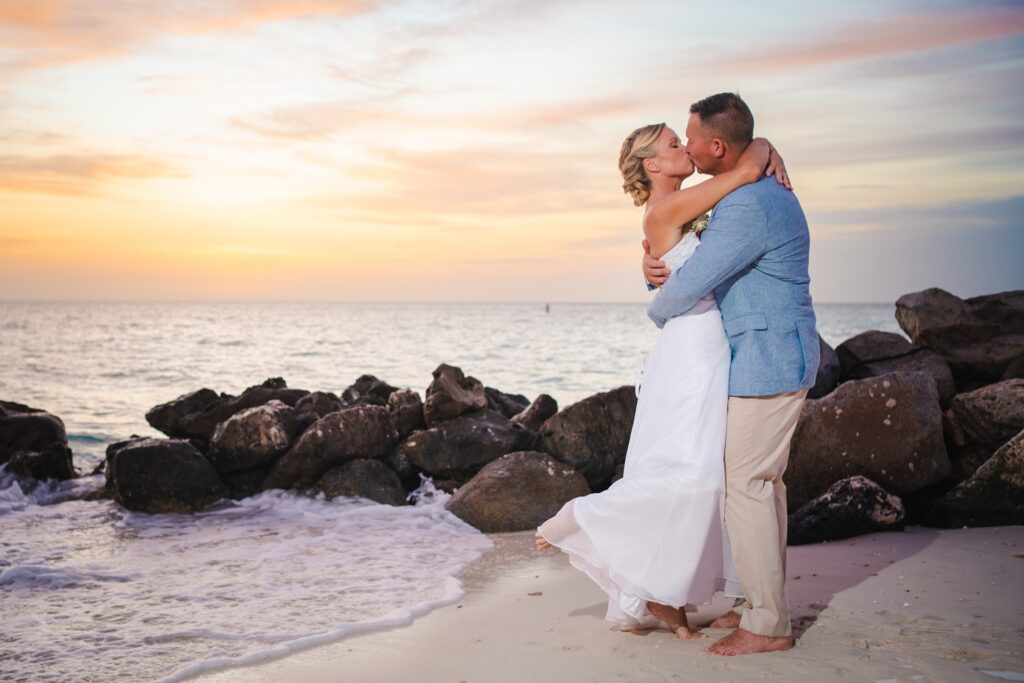 Bride and groom kissing near Aruba rocks on beach