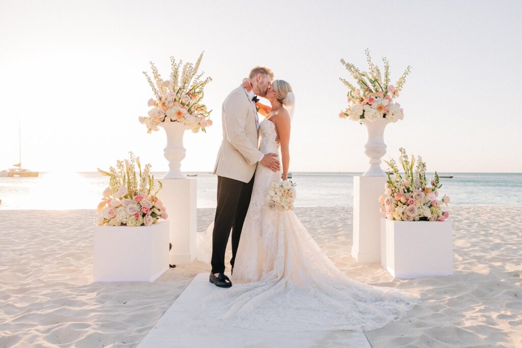 Bride and groom kissing near Aruba wedding floral pillars