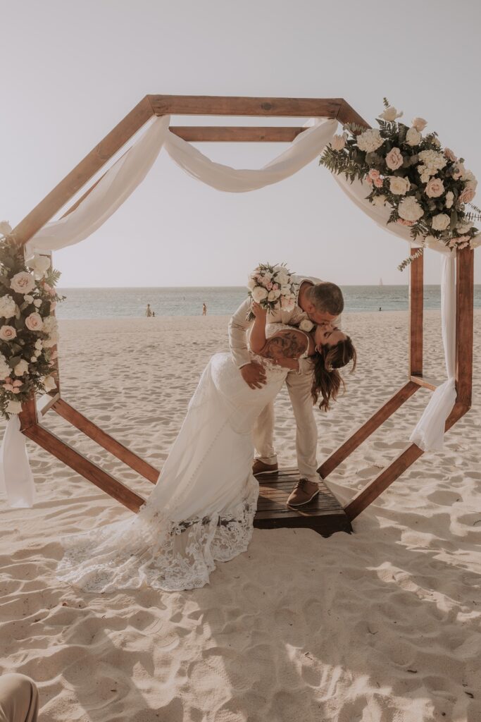 Groom dipping bride in ceremony arch on Aruba beach