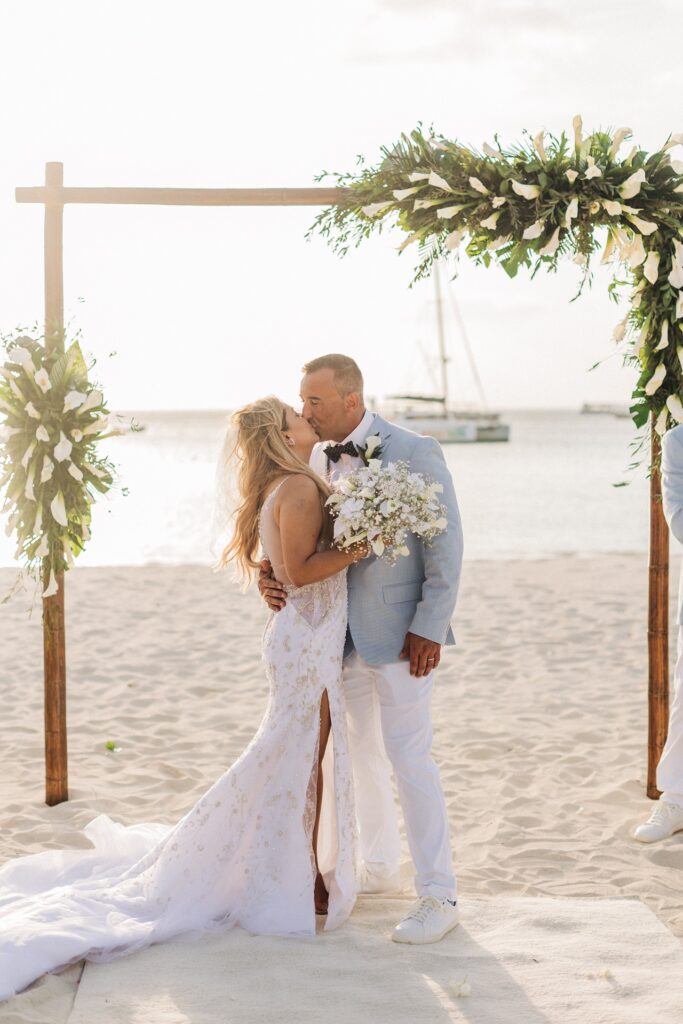 Bride and groom kissing under wooden arch at Aruba ceremony